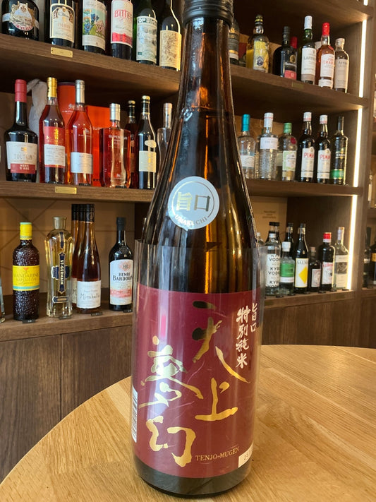 Tenjo Mugen Tokubetsu Junmai sake bottle with deep red label featuring gold and white Japanese calligraphy, artisan premium.