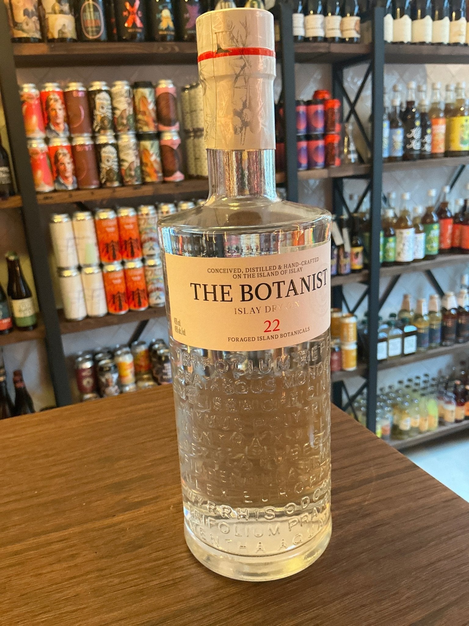 Clear glass bottle of The Botanist Islay Dry Gin with textured botanical design, sealed with natural cork and red wax,.