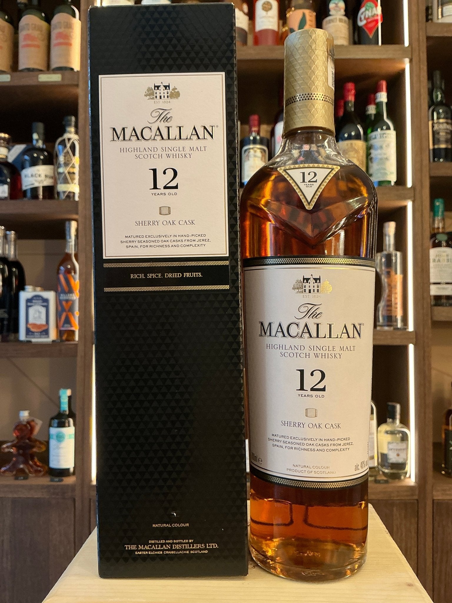 The Macallan 12 Year Old Sherry Oak Cask premium aged single malt whisky bottle with black textured box on wooden surface,.