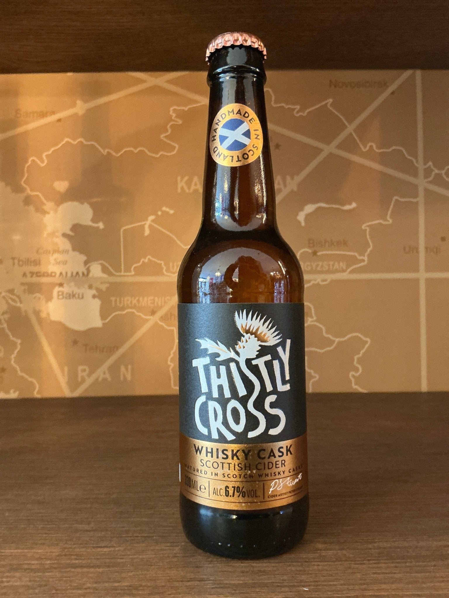 Dark amber glass bottle with black and white Thistly Cross label featuring a thistle illustration, copper foil cap, and gold