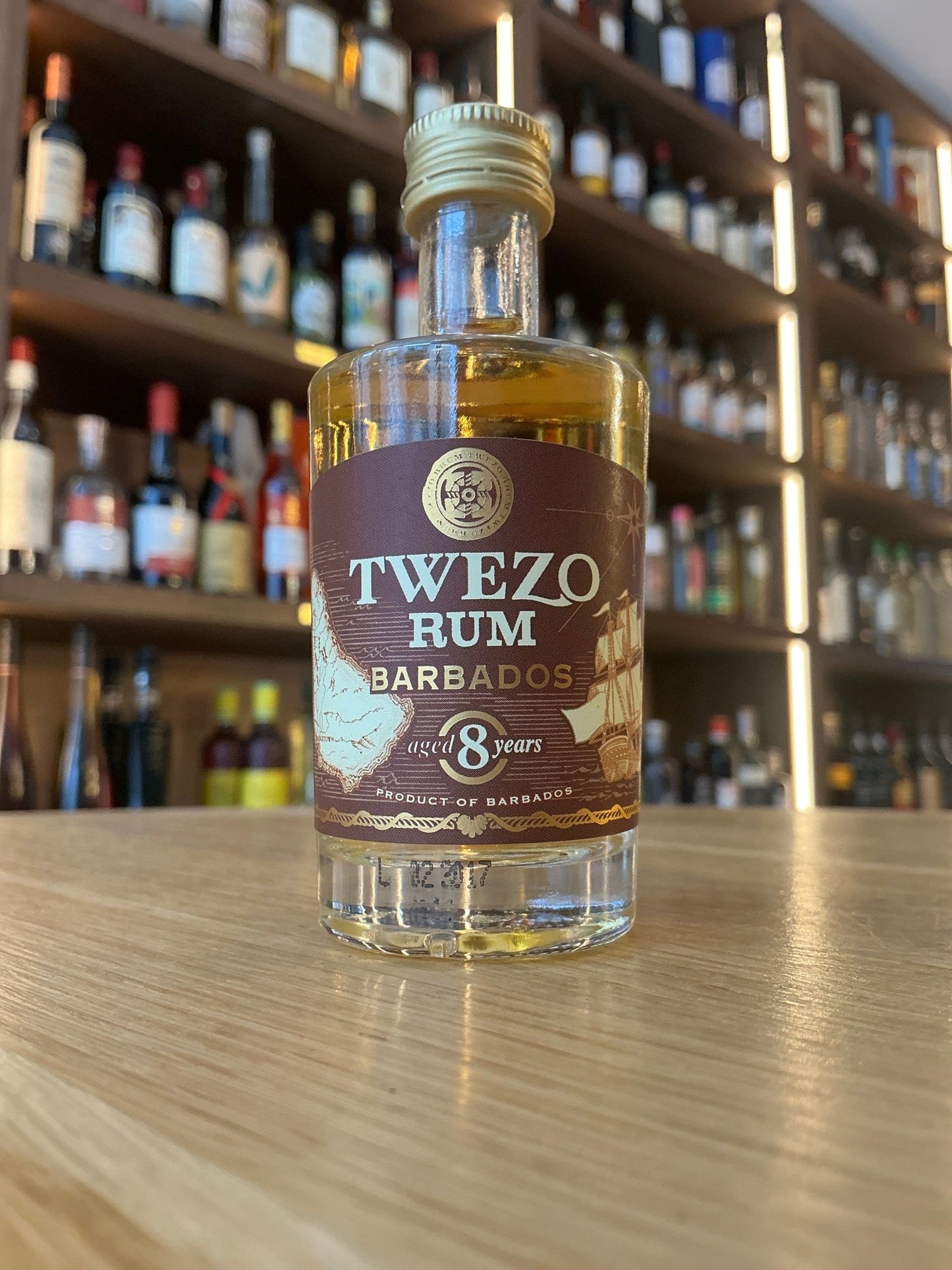 Small bottle of Twezo Rum Barbados 8 Years aged golden rum with premium artisan label on wooden surface, shelves of.