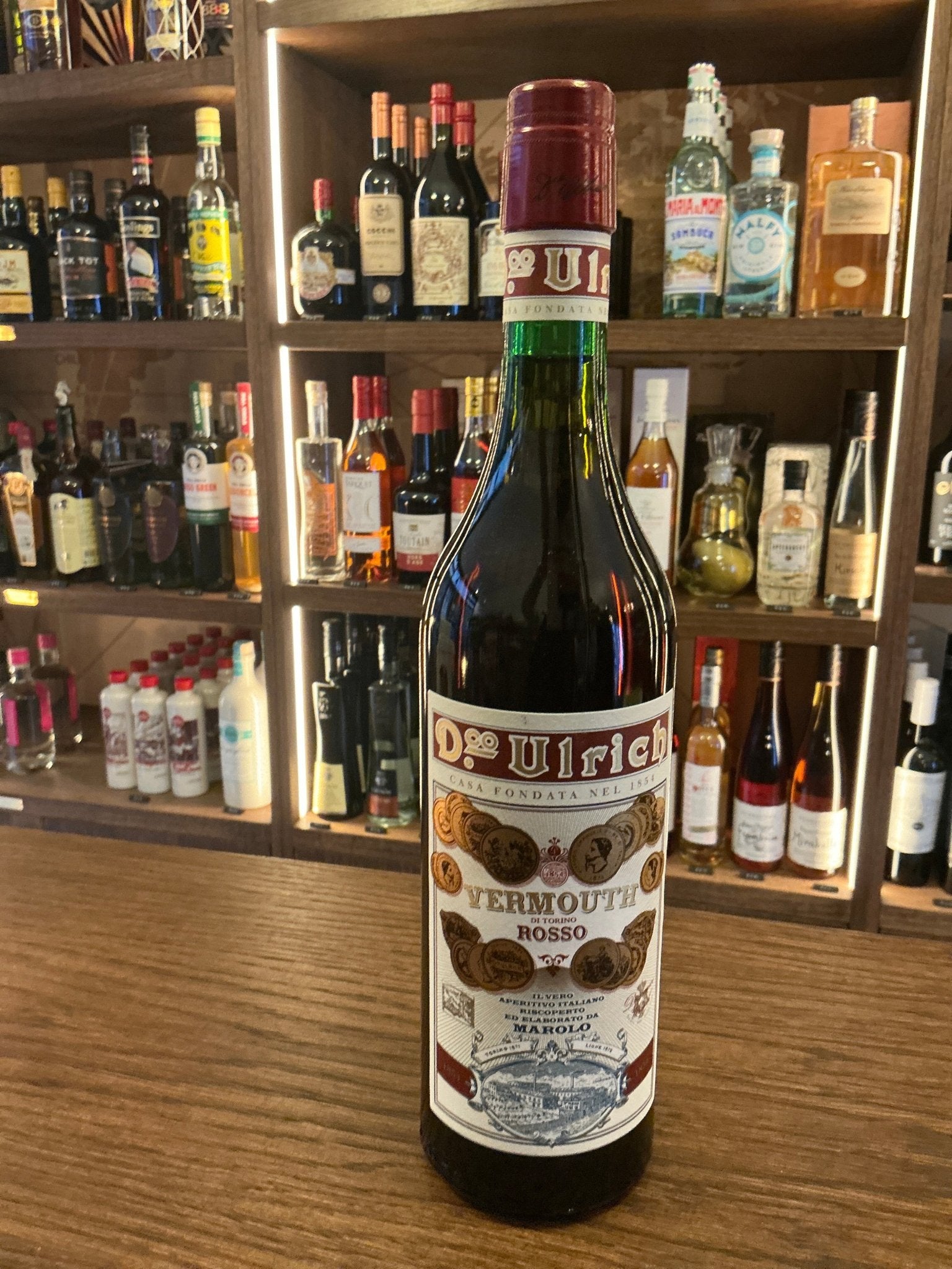 Ulrich Rosso red vermouth bottle with spiced, botanical label on wooden bar showcasing premium Italian specialty spirit.