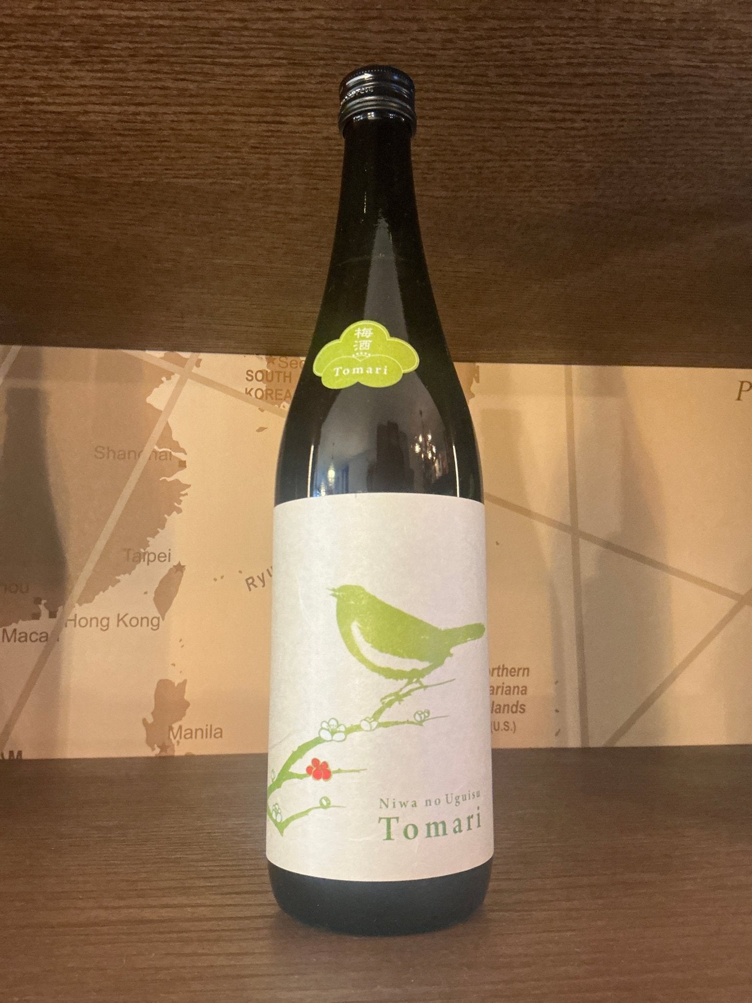 Tall dark glass bottle of Usuisu Ume-shu Tomari plum liqueur with artisanal label featuring green bird illustration, premium .