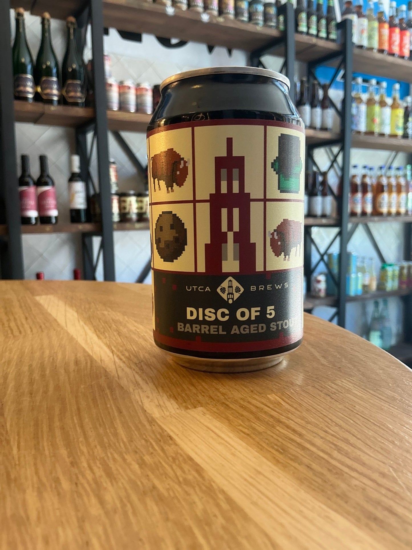 UTCA Disc Of 5 Barrel Aged stout can with botanical and spiced label design on wooden table in craft beer shop.