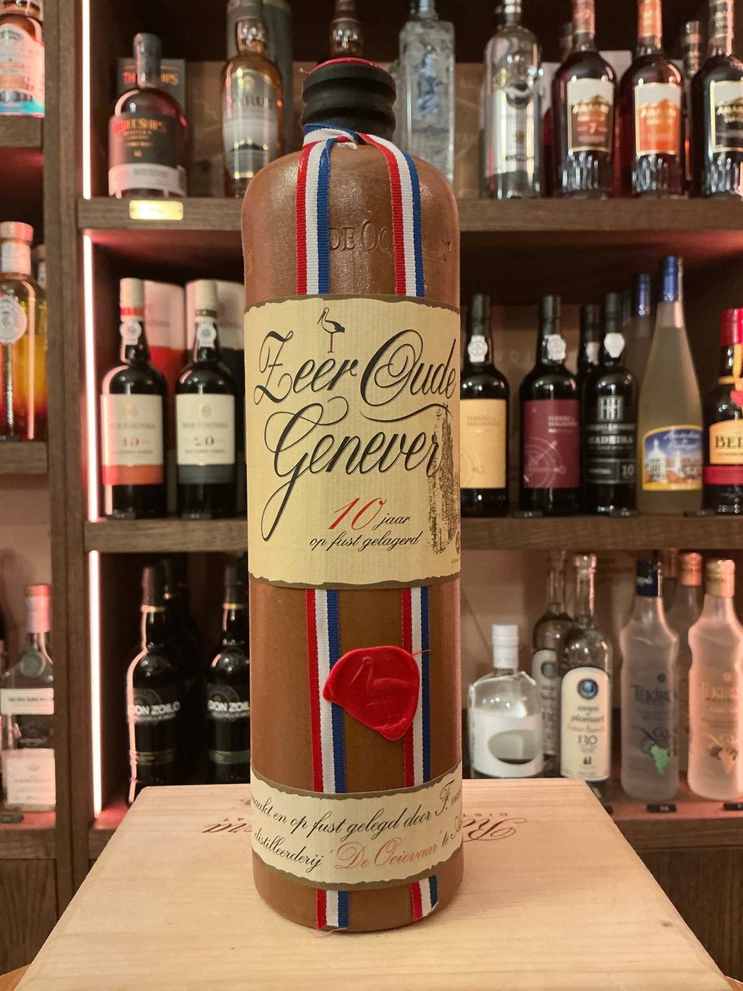 Van Wees Zeer Oude Genever 10 Year aged Dutch gin with botanical, spiced flavor in tall glass bottle with tricolor ribbon.