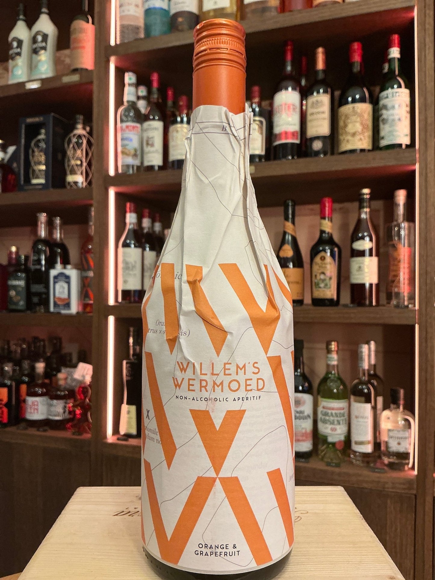Willem's Wermoed bottle wrapped in white and orange paper with bold geometric design on bar counter, premium Dutch artisanal .