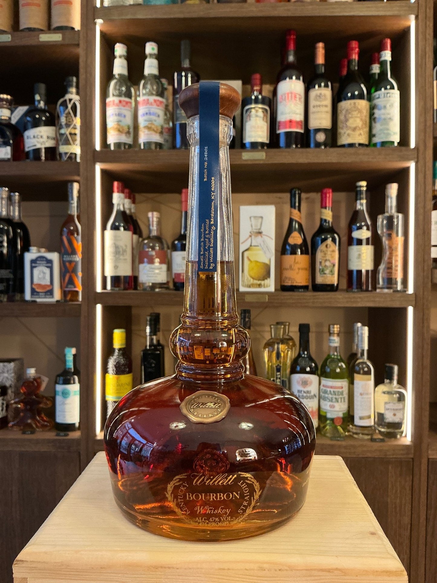 Willet Pot Still Reserve bourbon bottle with amber liquid, embossed round base, long neck, and gold accents on wooden table, .