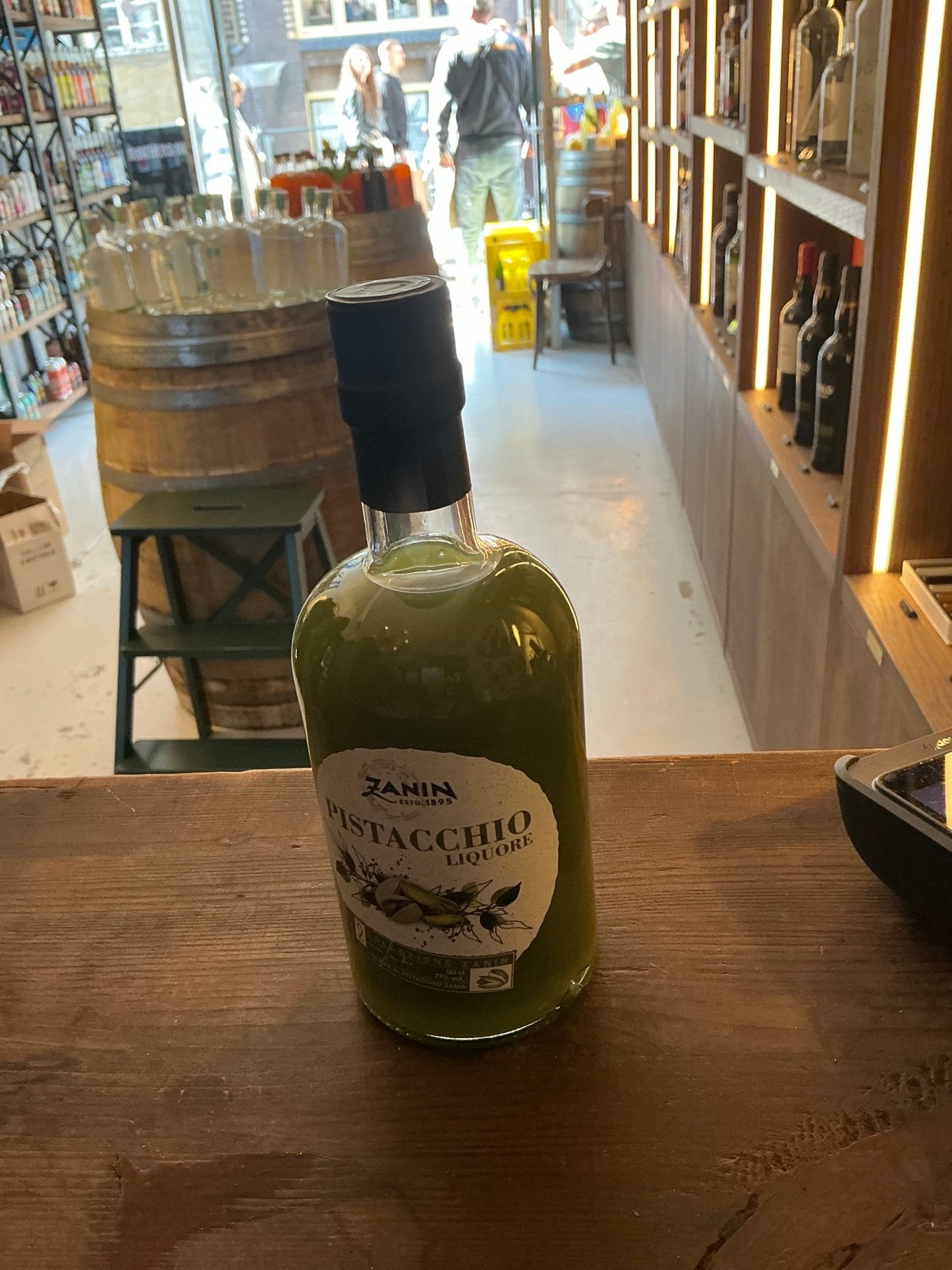 Zanin Pistacchio Liqueur in clear glass bottle with black cap, green nut-based premium artisan liqueur on wooden counter in.