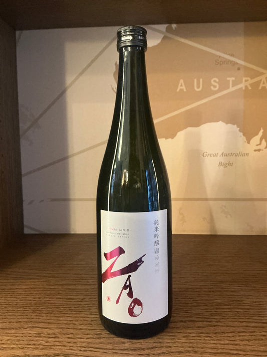 Tall green glass bottle of Zao Junmai Ginjo sake with white label featuring bold red and black calligraphy, standing on.